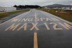 A wet taxiway labeled with the words Wingspan Max 12M at Canberra Airport in August 2020. Taxiway and unserviceability cones appear on the grass next to the taxiway.