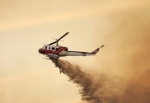 Fire fighting helicopter dropping water against a smoky orange sky.