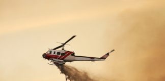 Fire fighting helicopter dropping water against a smoky orange sky.