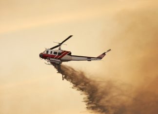 Fire fighting helicopter dropping water against a smoky orange sky.