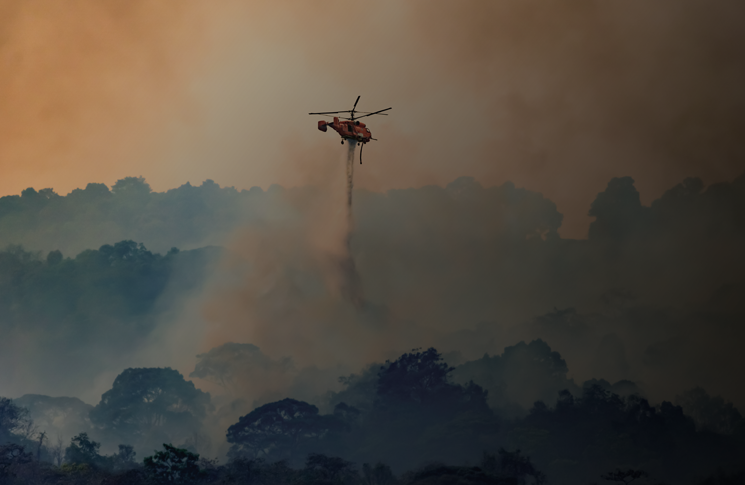 Helicopter water bomber putting out fires in a bushland environment