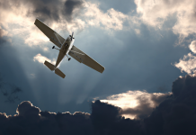 Image of a small plane flying out of dark clouds with some sunlight