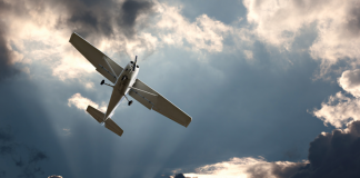 Image of a small plane flying out of dark clouds with some sunlight