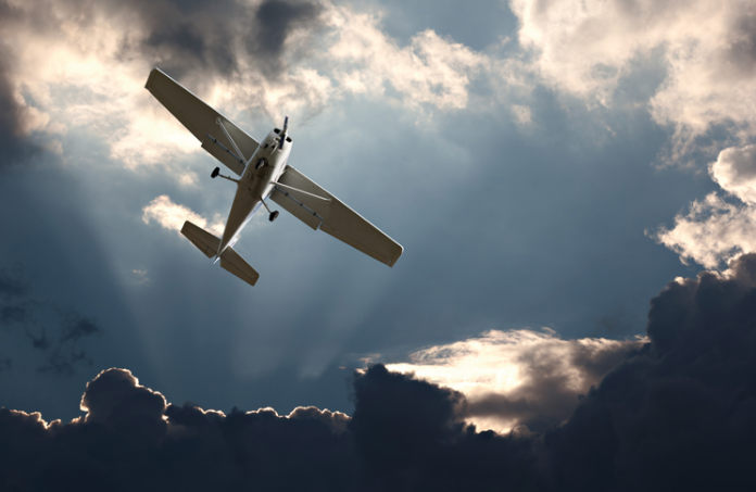 Image of a small plane flying out of dark clouds with some sunlight