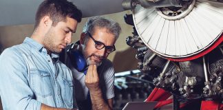 aircraft engineers working on aircraft, referring to and discussing information on a laptop device.