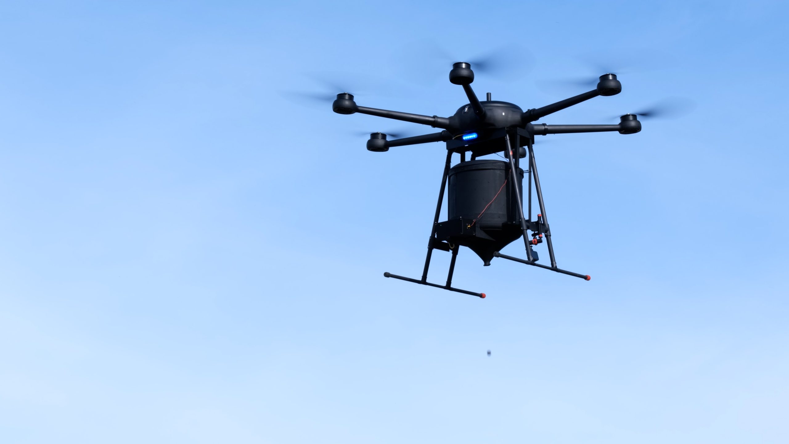 An AirSeed drone mid-flight dropping a seed pod