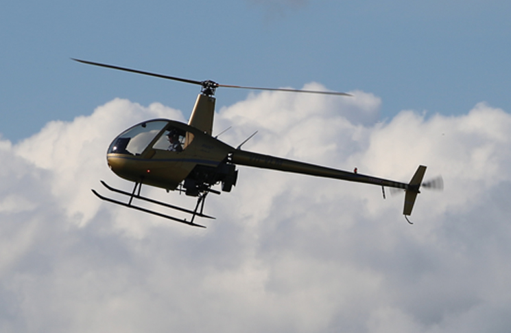 Robinson R22 helicopter flying with clouds in the background