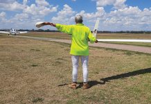 Photo of person holding the wing tip of a glider and signalling a tug with their arm.