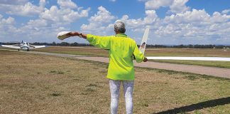 Photo of person holding the wing tip of a glider and signalling a tug with their arm.