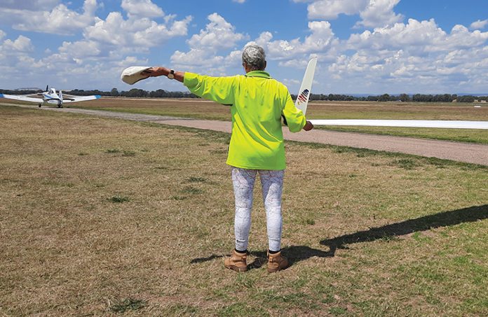 Photo of person holding the wing tip of a glider and signalling a tug with their arm.