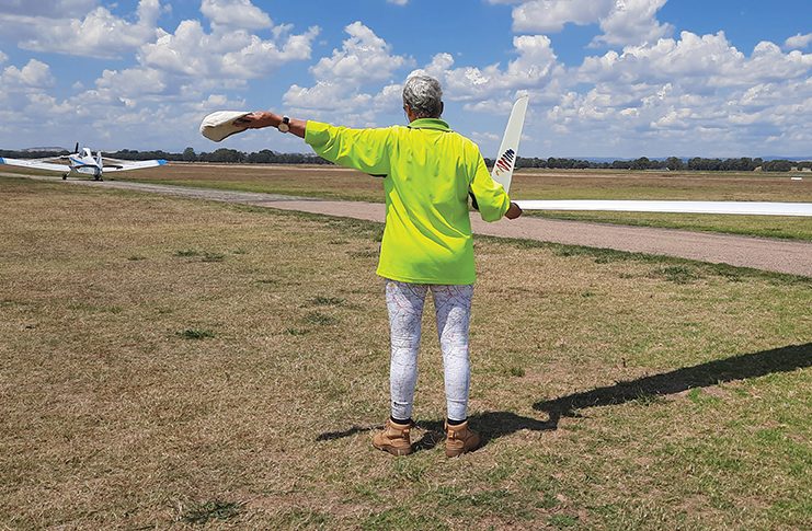 Photo of person holding the wing tip of a glider and signalling a tug with their arm.