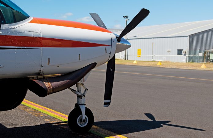 Photo of the front of a small aircraft with a propellor on the tarmac