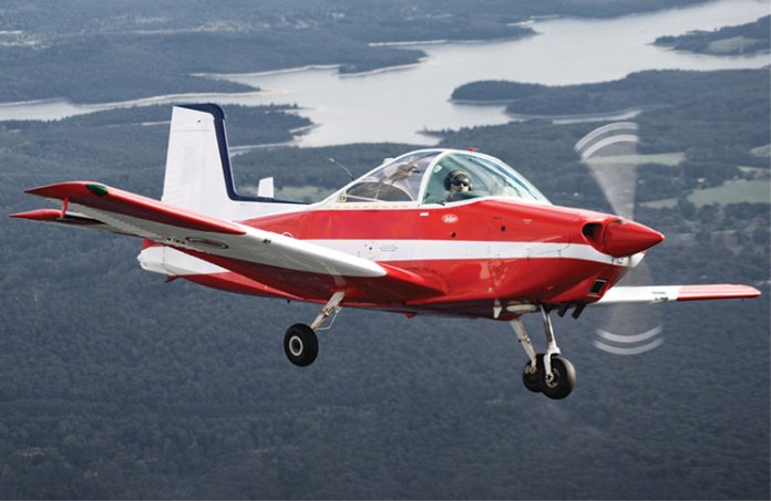 Photo of small red and white aircraft flying with land and water in the background