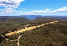 An unsealed runway surrounded by bushland. A blue sky with scattered above.