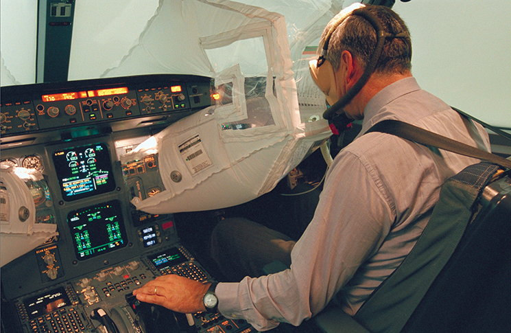 Photo of a pilot in a cockpit using an emergency vision assurance system allows a pilot to see instrument displays and through windows in a smoke-filled flight deck