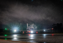 Light aircraft with headlights on sits on a wet runway at night in rain.