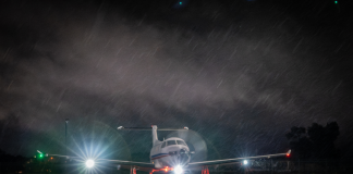 Light aircraft with headlights on sits on a wet runway at night in rain.