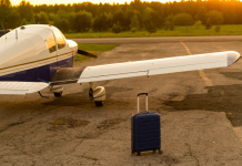A blue suitcase and a parked small private jet. Quadruple plane with a propeller for an air taxi in the sunset.