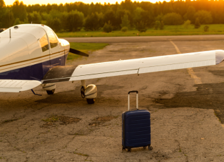 A blue suitcase and a parked small private jet. Quadruple plane with a propeller for an air taxi in the sunset.