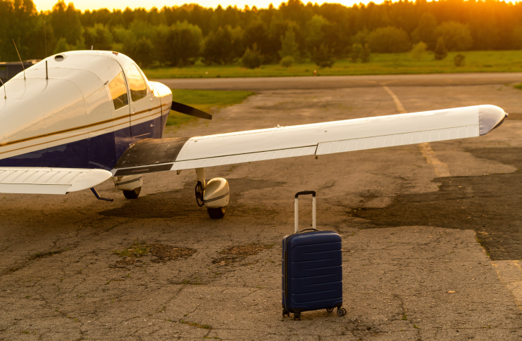 A blue suitcase and a parked small private jet. Quadruple plane with a propeller for an air taxi in the sunset.