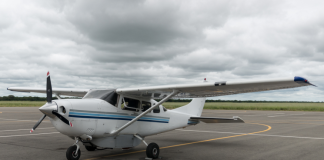 A white Cessna 206 parked on an apron under a cloudy sky.