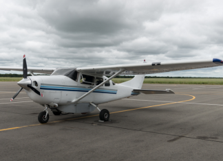 A white Cessna 206 parked on an apron under a cloudy sky.
