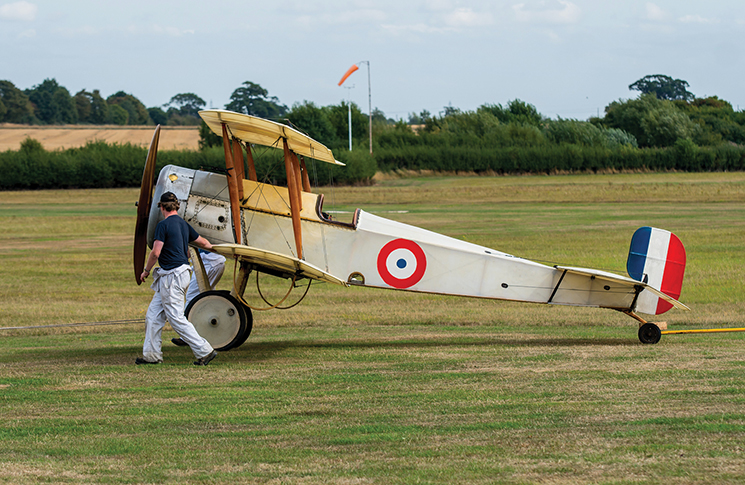 A man is walking next to a small biplane on a grassy field.