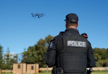 A police officer is watching a drone flying in the sky.