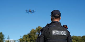 A police officer is watching a drone flying in the sky.