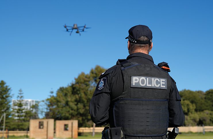 A police officer is watching a drone flying in the sky.