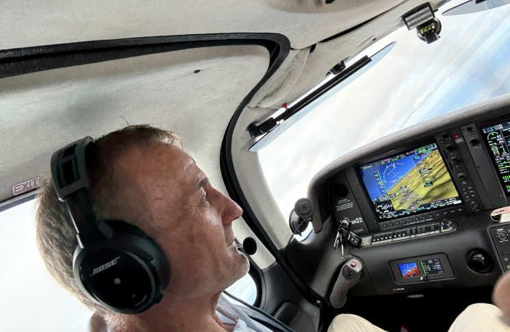 Pilot wearing a headset in a light aircraft cockpit, looking ahead while using onboard navigation displays during flight.