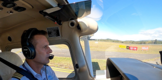 Pilot in a light aircraft cockpit at a controlled aerodrome, wearing a headset and preparing for taxi, with the runway visible ahead.