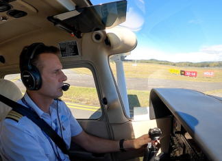 Pilot in a light aircraft cockpit at a controlled aerodrome, wearing a headset and preparing for taxi, with the runway visible ahead.