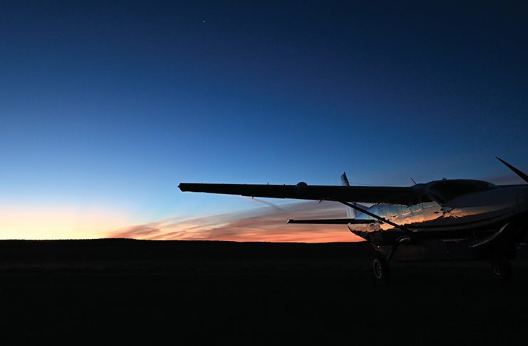 A plane is parked on the ground with a sunset behind it.