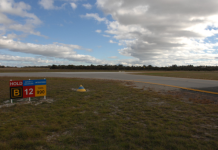 View of taxiway B and runway 12 at Jandakot Aerodrome, showing a runway holding point sign and the intersection area where pilots must maintain situational awareness while taxiing.