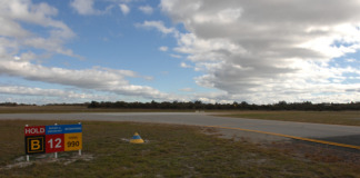 View of taxiway B and runway 12 at Jandakot Aerodrome, showing a runway holding point sign and the intersection area where pilots must maintain situational awareness while taxiing.
