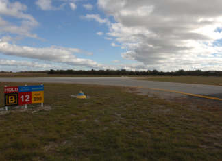View of taxiway B and runway 12 at Jandakot Aerodrome, showing a runway holding point sign and the intersection area where pilots must maintain situational awareness while taxiing.