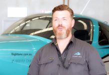 Man with beard in blue shirt standing on the side of green aeroplane