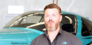Man with beard in blue shirt standing on the side of green aeroplane