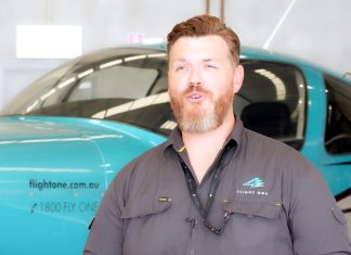 Man with beard in blue shirt standing on the side of green aeroplane