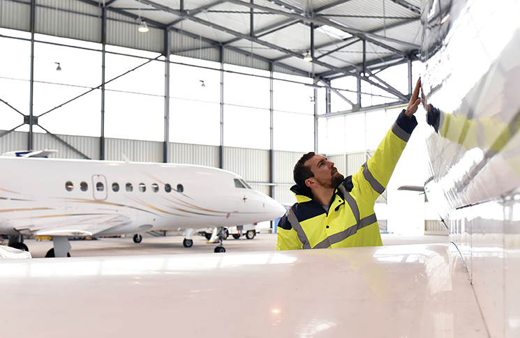A person in a high-visibility vest inspecting an aeroplane in a hangar