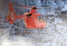 A helicopter flying with snowy trees in the background