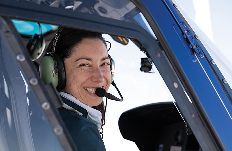 A female pilot sitting in the cockpit of an aircraft and smiling