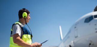 Side view of airport worker in a high visibility vest looking at passenger plane.