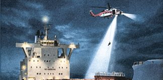 A helicopter hovers above a ship at night, as a light beams down and someone descends on a rope