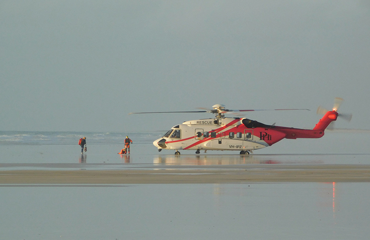 A helicopter landed on the beach, with people walking towards it