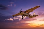 A small aeroplane is flying against a colourful sky at sunset with scattered clouds