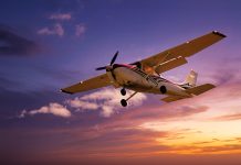 A small aeroplane is flying against a colourful sky at sunset with scattered clouds