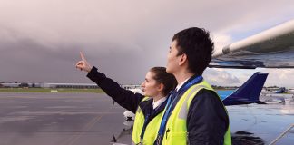 Two people in high visibility jackets with aeroplanes behind them