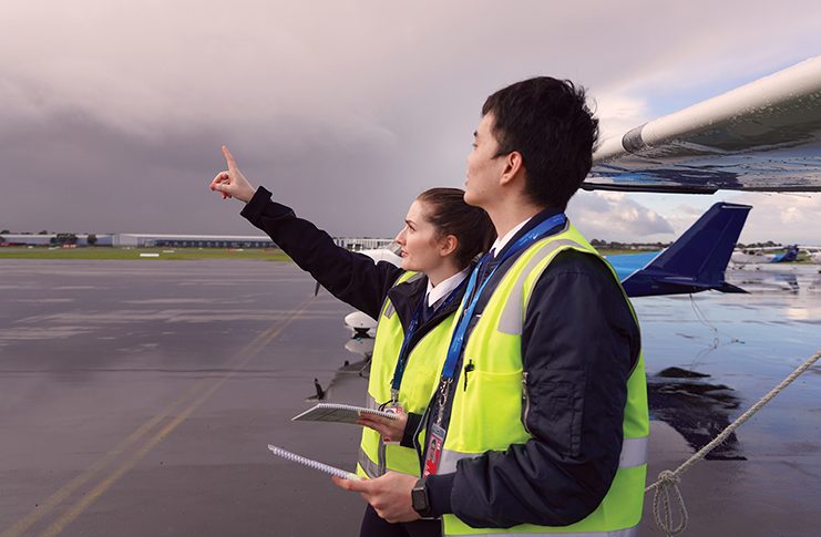Future tense Two people in high visibility jackets with aeroplanes behind them